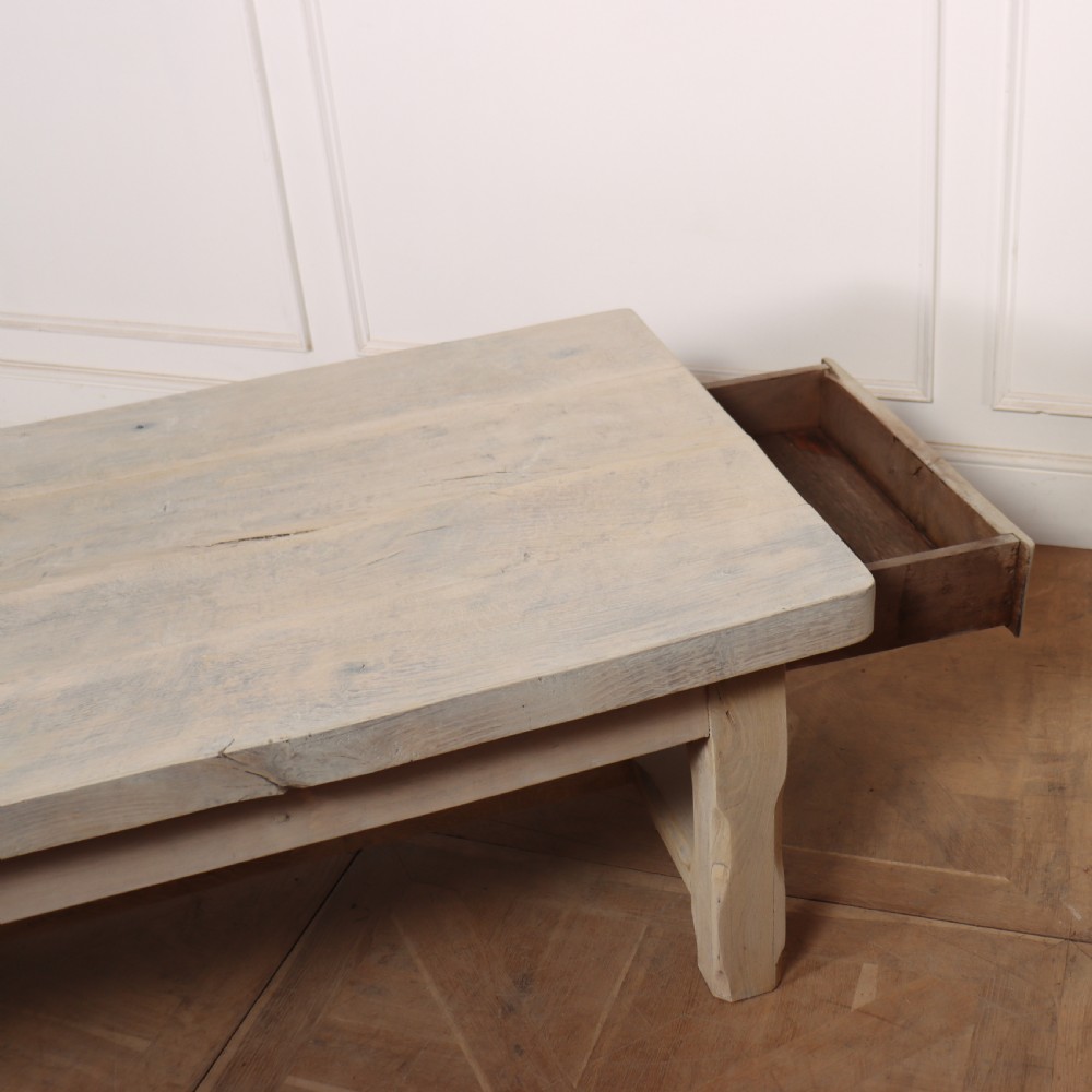 A low rectangular French coffee table constructed from bleached oak, featuring a thick plank top, square legs, a low stretcher, and a small end drawer. View VI