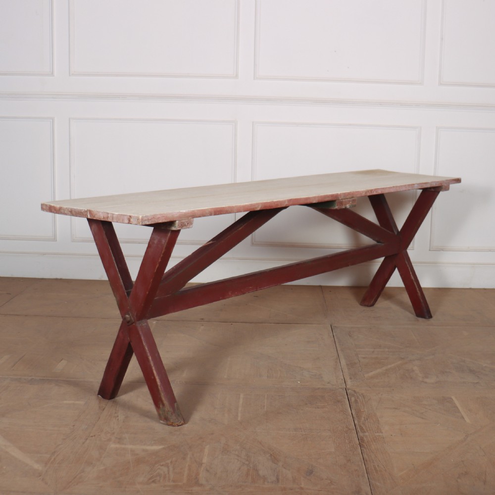 A long wooden tavern table featuring a light scrubbed timber top supported by a red painted X-frame trestle base.