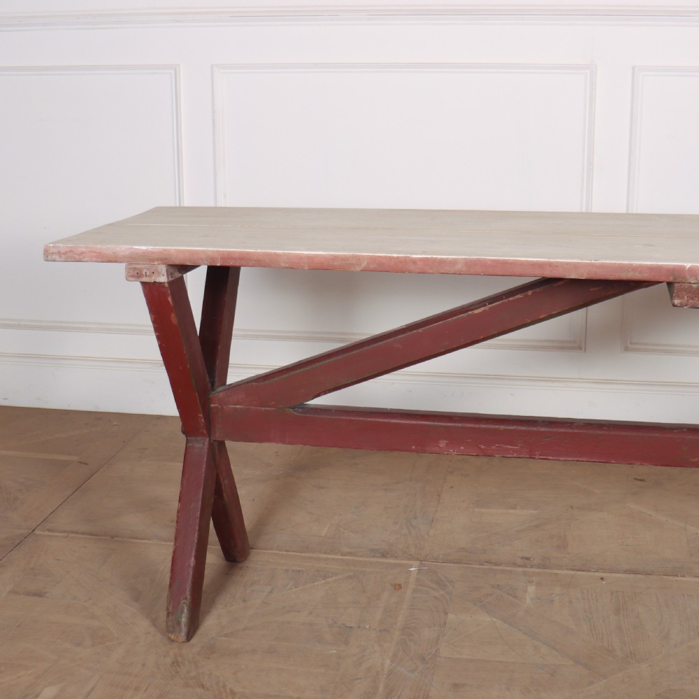 A long wooden tavern table featuring a light scrubbed timber top supported by a red painted X-frame trestle base. View II