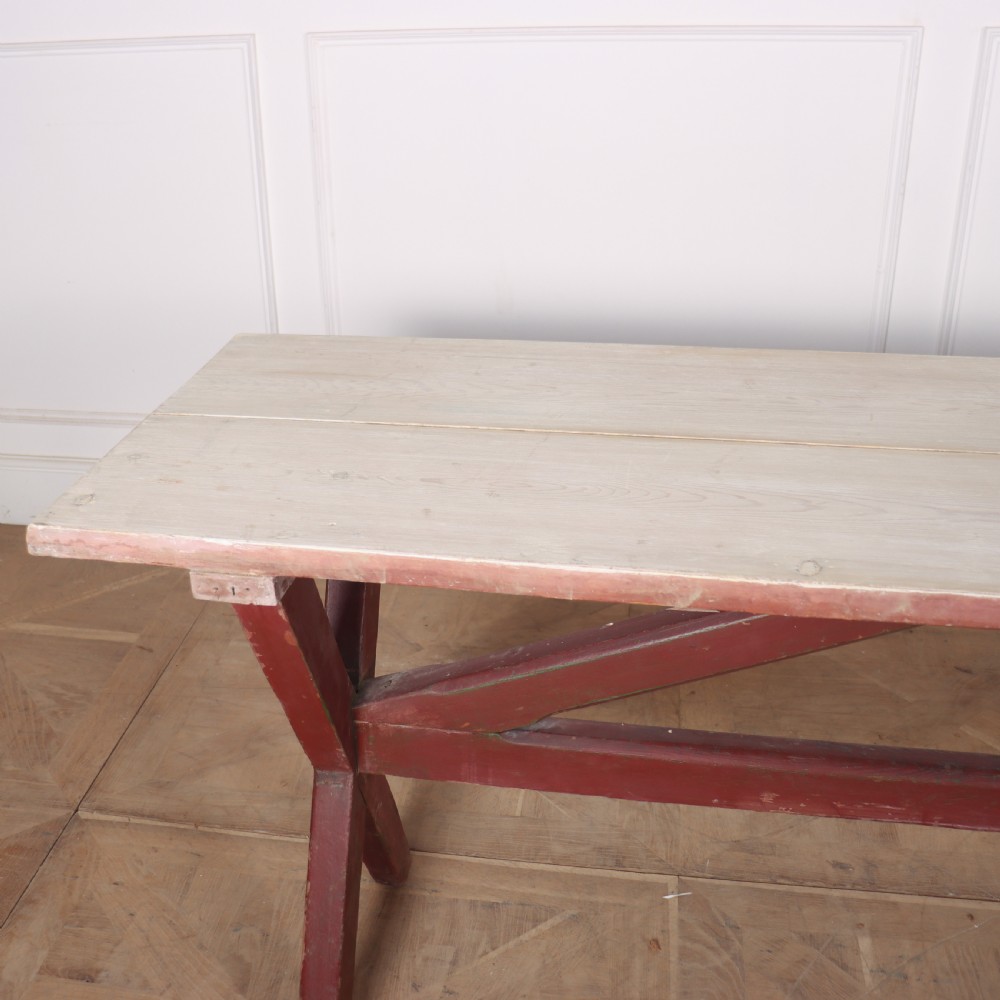 A long wooden tavern table featuring a light scrubbed timber top supported by a red painted X-frame trestle base. View IV