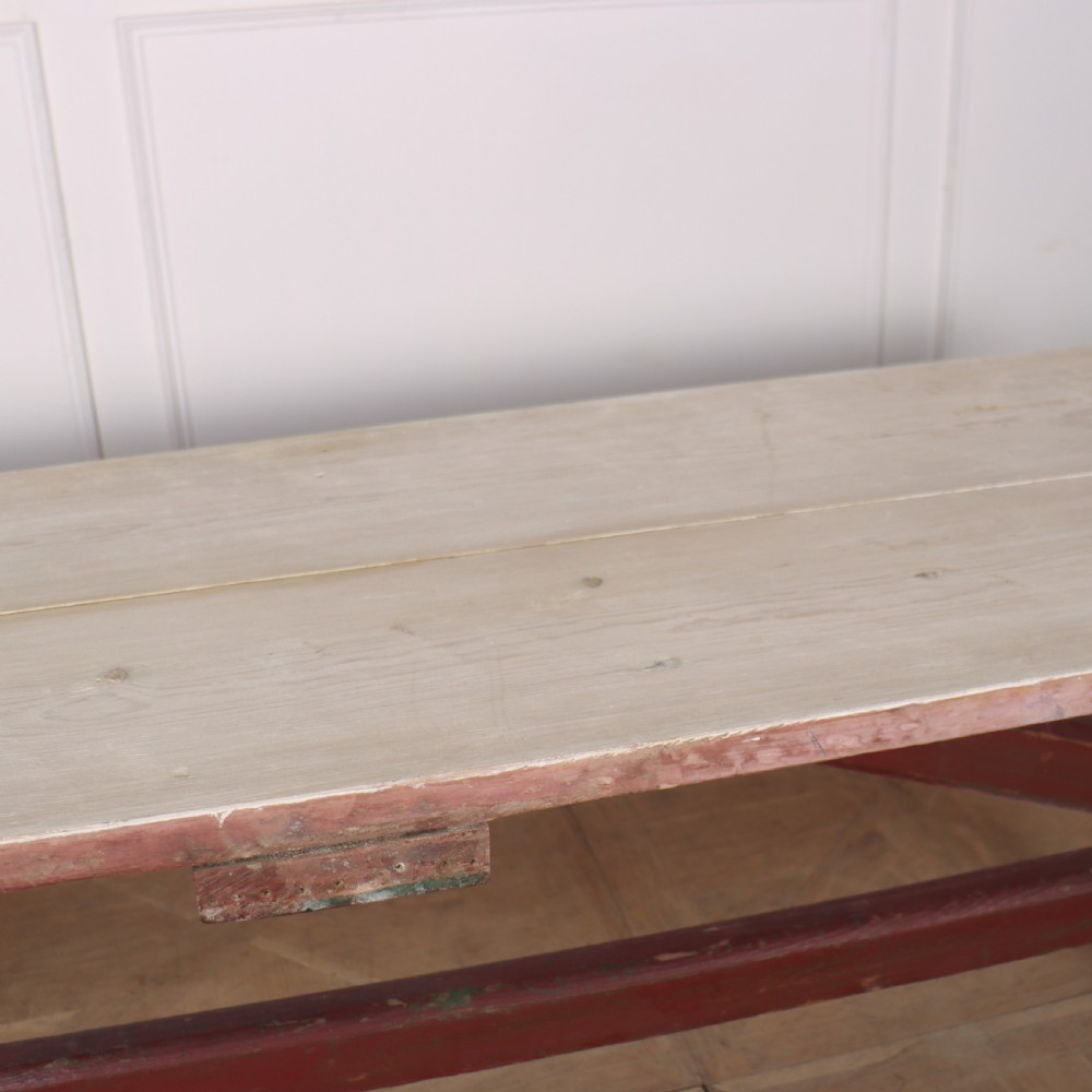 A long wooden tavern table featuring a light scrubbed timber top supported by a red painted X-frame trestle base. View V