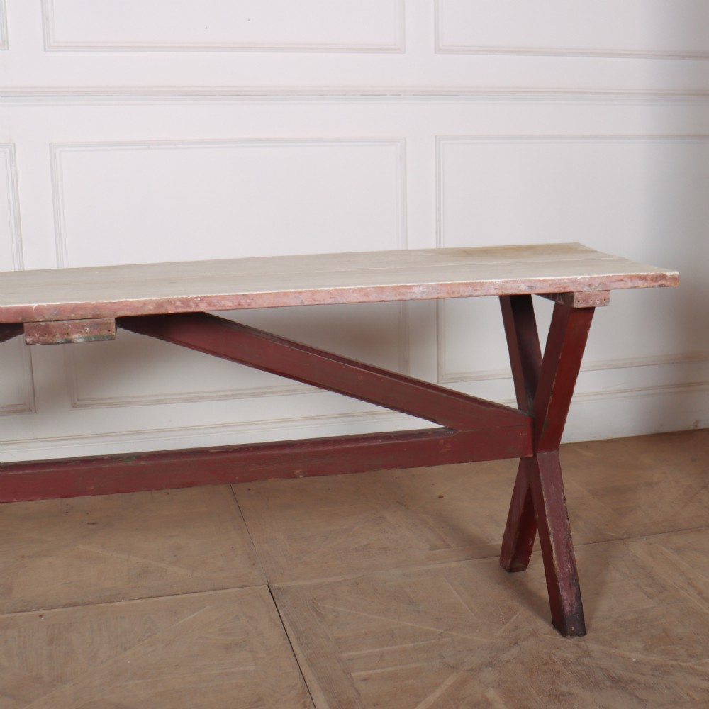 A long wooden tavern table featuring a light scrubbed timber top supported by a red painted X-frame trestle base. View VI