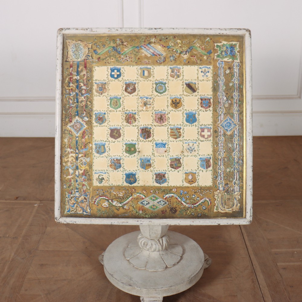 A square painted lamp table featuring a grid of heraldic coats of arms on a cream ground, supported by a carved off-white pedestal base.