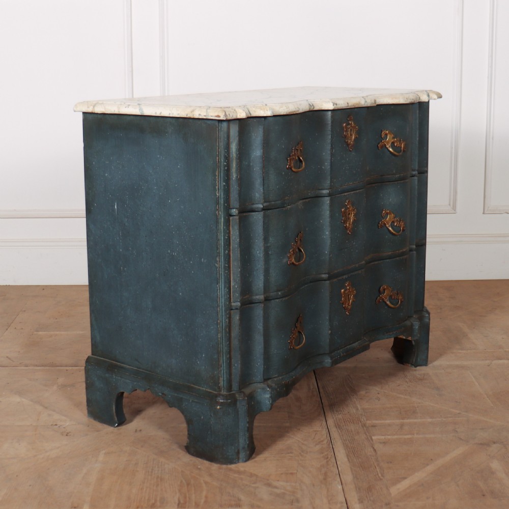 An 18th-century Dutch painted commode featuring a blue serpentine-front wooden body, three drawers with ornamental brass handles, and a contoured white marble top.