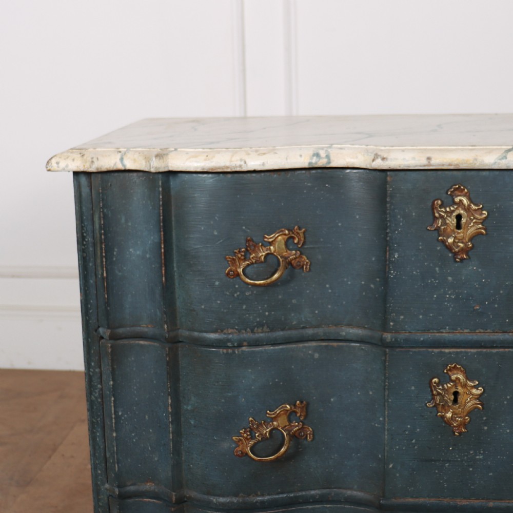 An 18th-century Dutch painted commode featuring a blue serpentine-front wooden body, three drawers with ornamental brass handles, and a contoured white marble top. View V
