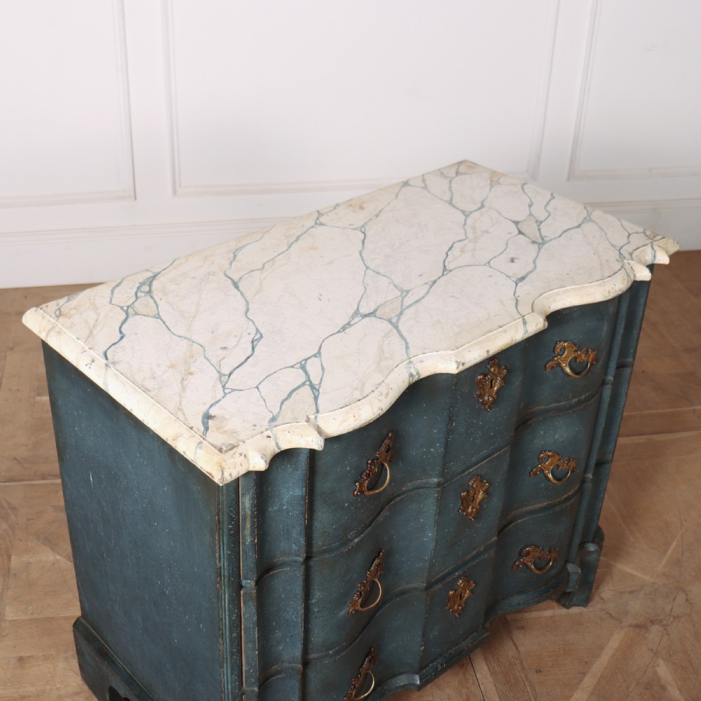 An 18th-century Dutch painted commode featuring a blue serpentine-front wooden body, three drawers with ornamental brass handles, and a contoured white marble top. View IX