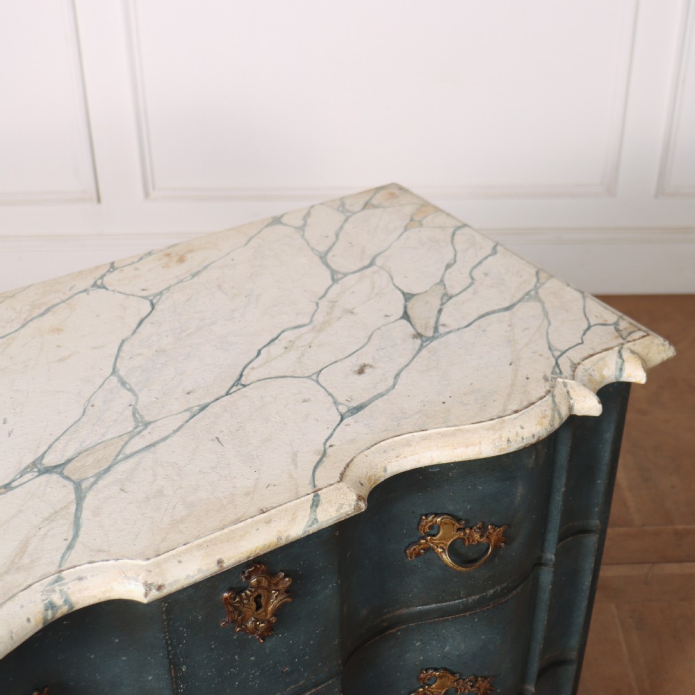 An 18th-century Dutch painted commode featuring a blue serpentine-front wooden body, three drawers with ornamental brass handles, and a contoured white marble top. View X