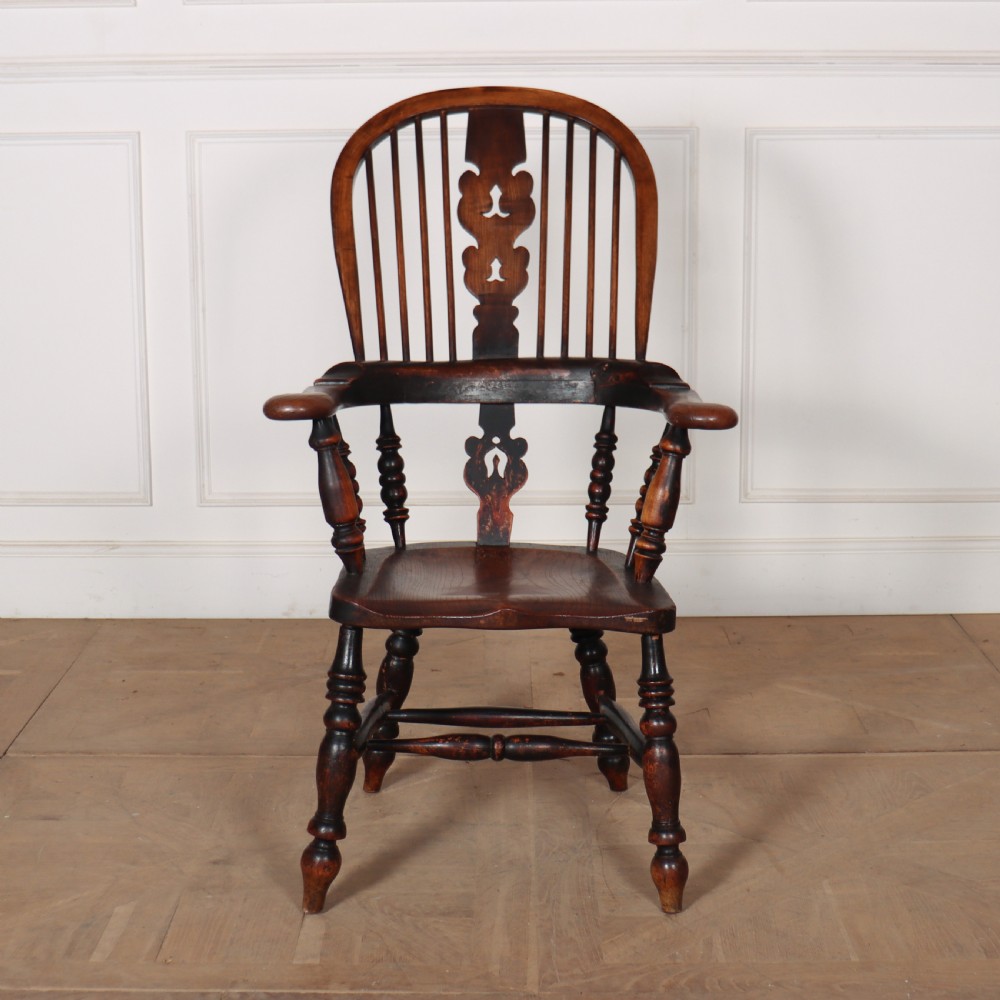 An antique dark wood Yorkshire Windsor armchair featuring a hoop back with a central pierced splat, slender spindles, broad armrests, and turned legs.
