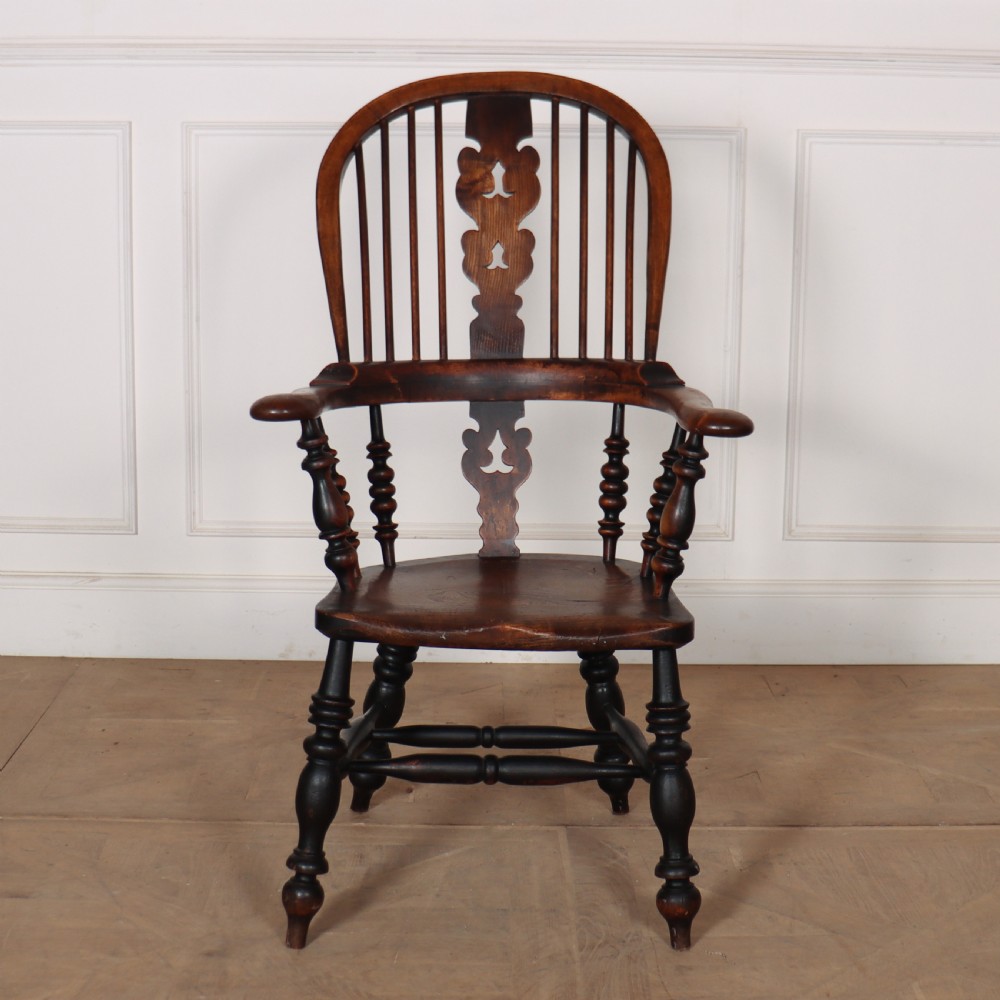 A 19th-century dark brown wood Yorkshire Windsor armchair featuring a hoop back, pierced central splat, turned legs, and curved armrests.
