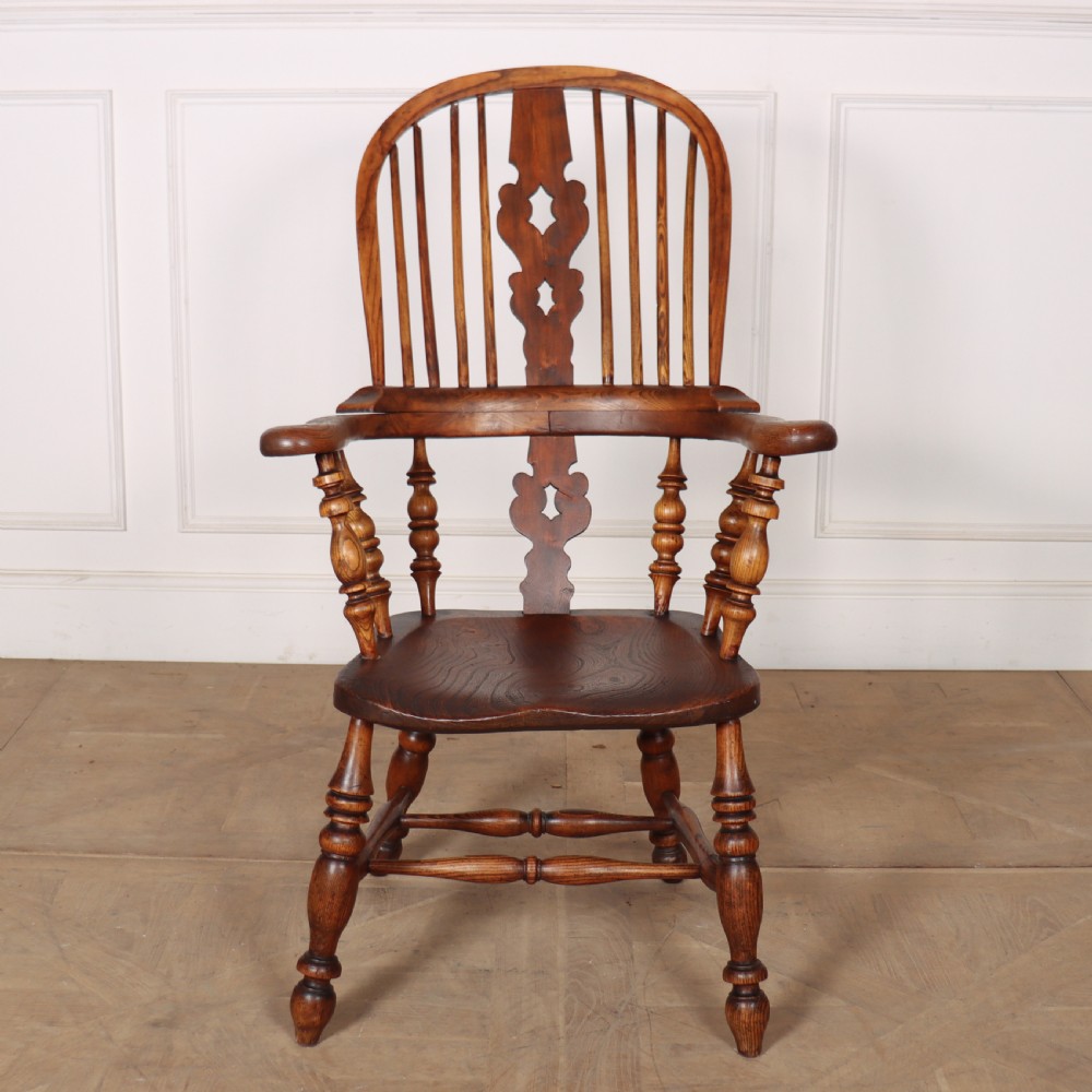 A warm brown wooden Windsor armchair featuring a hoop back, pierced central splat, turned spindles, a contoured seat, and turned legs with stretchers.