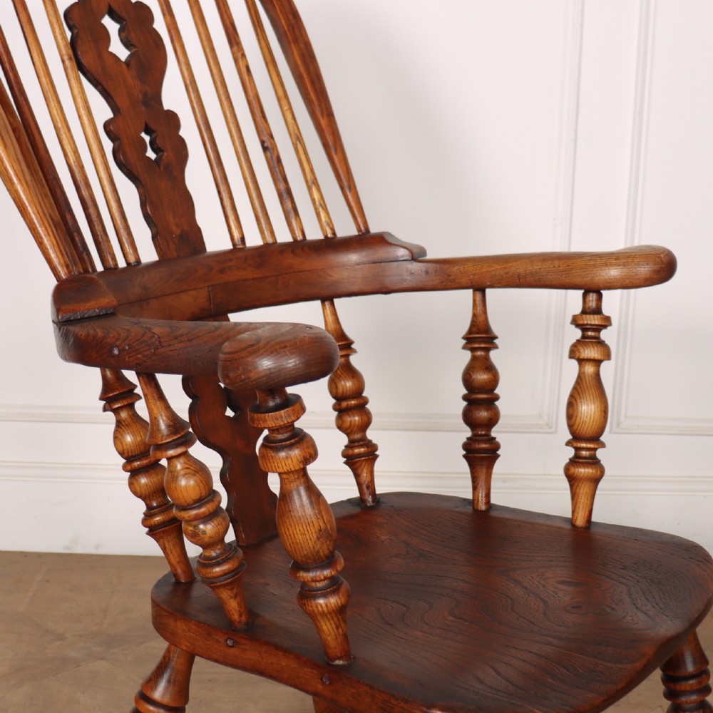 A warm brown wooden Windsor armchair featuring a hoop back, pierced central splat, turned spindles, a contoured seat, and turned legs with stretchers. View III