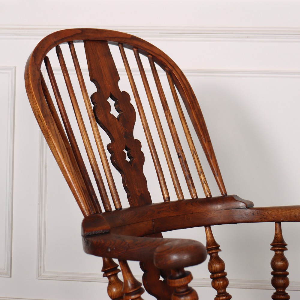 A warm brown wooden Windsor armchair featuring a hoop back, pierced central splat, turned spindles, a contoured seat, and turned legs with stretchers. View V