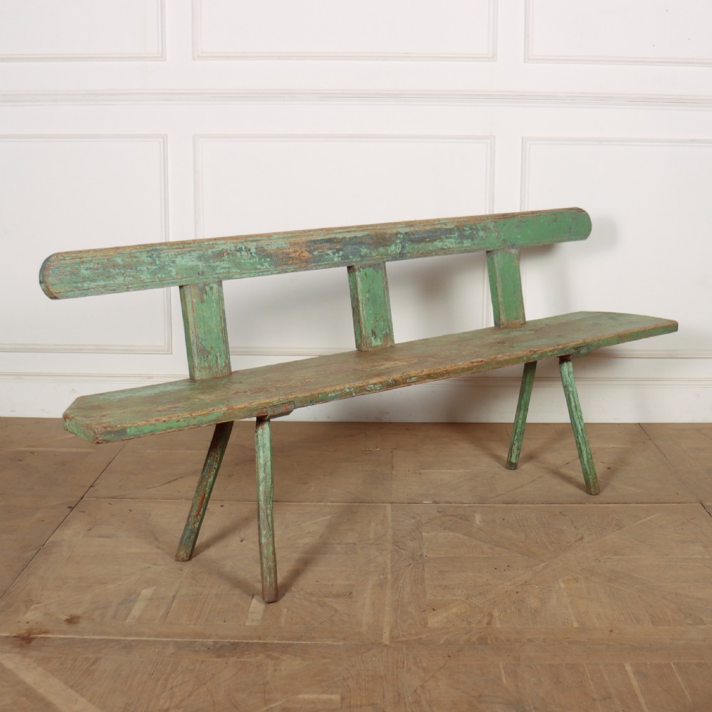 A long rustic wooden bench featuring distressed green paintwork, a simple narrow backrest, and four splayed legs.