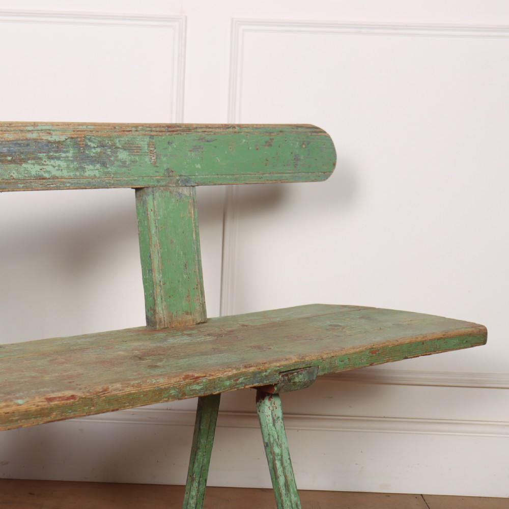 A long rustic wooden bench featuring distressed green paintwork, a simple narrow backrest, and four splayed legs. View III
