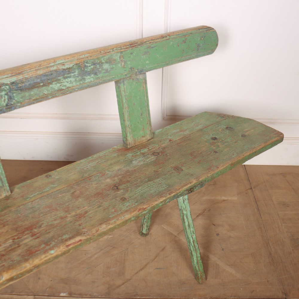 A long rustic wooden bench featuring distressed green paintwork, a simple narrow backrest, and four splayed legs. View IV