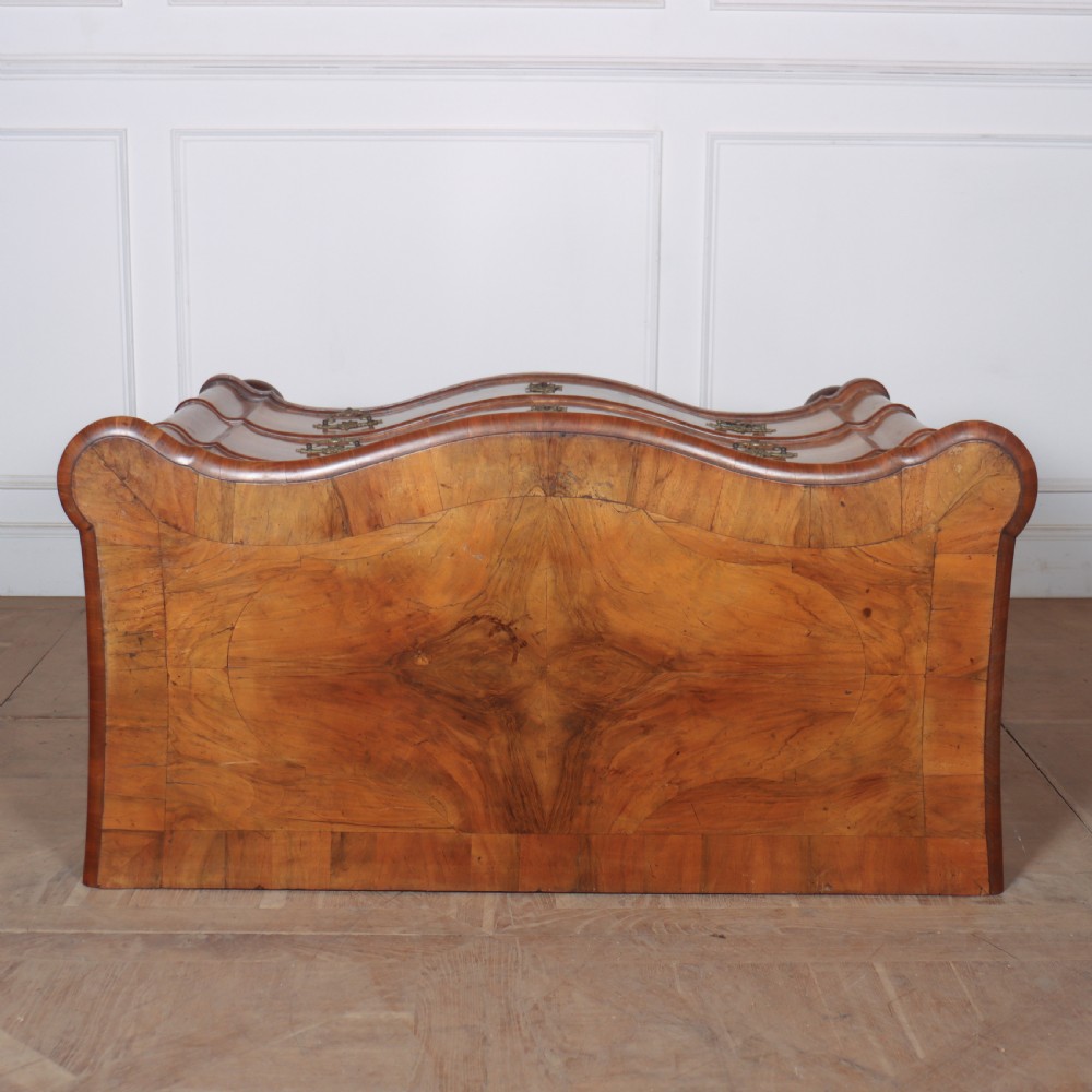 An 18th-century walnut serpentine commode featuring three long drawers with ornate brass handles and keyhole escutcheons, standing on turned bun feet. View VIII