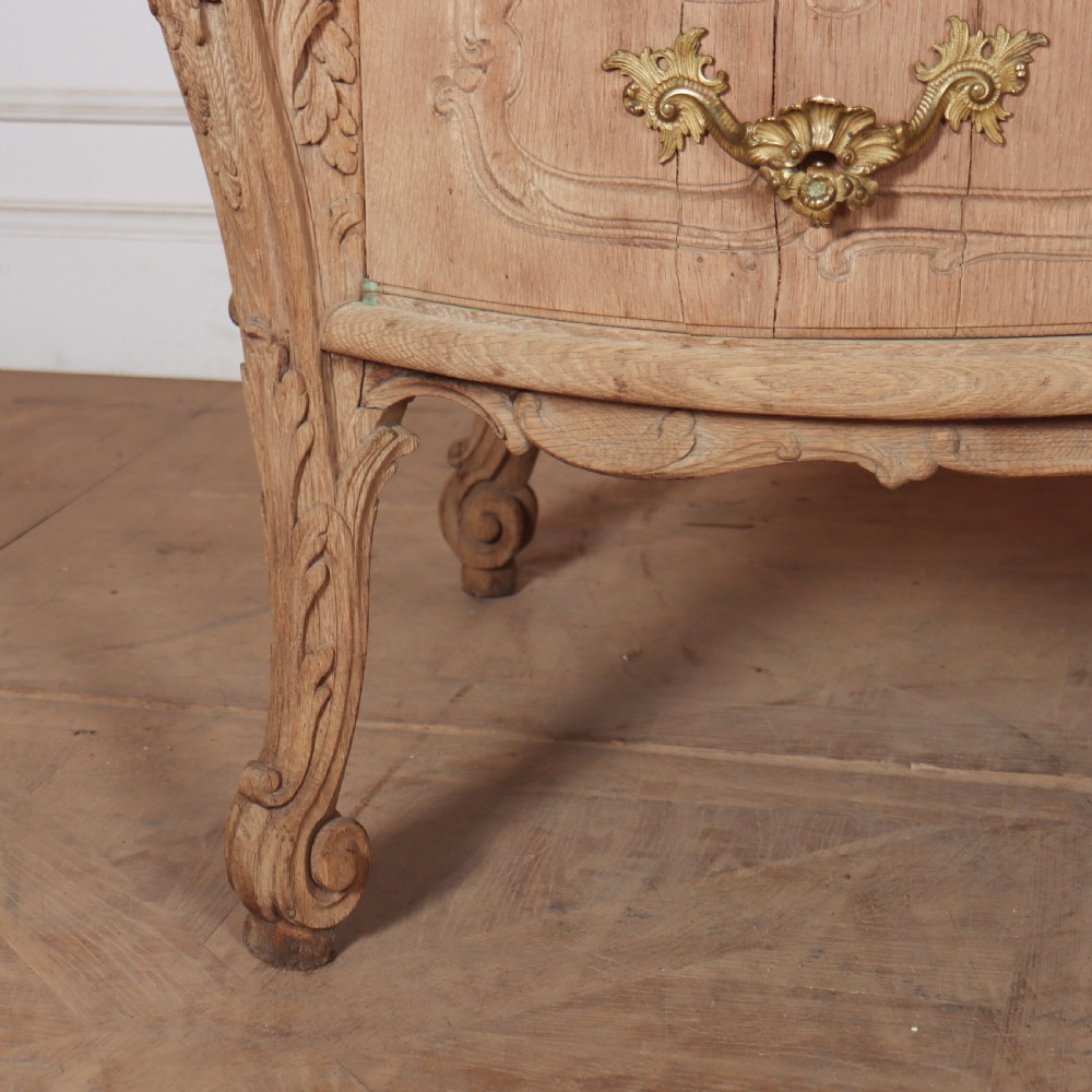 An antique French bleached oak commode featuring a serpentine front, carved rocaille mouldings, drawers with brass pulls, and cabriole feet. View II