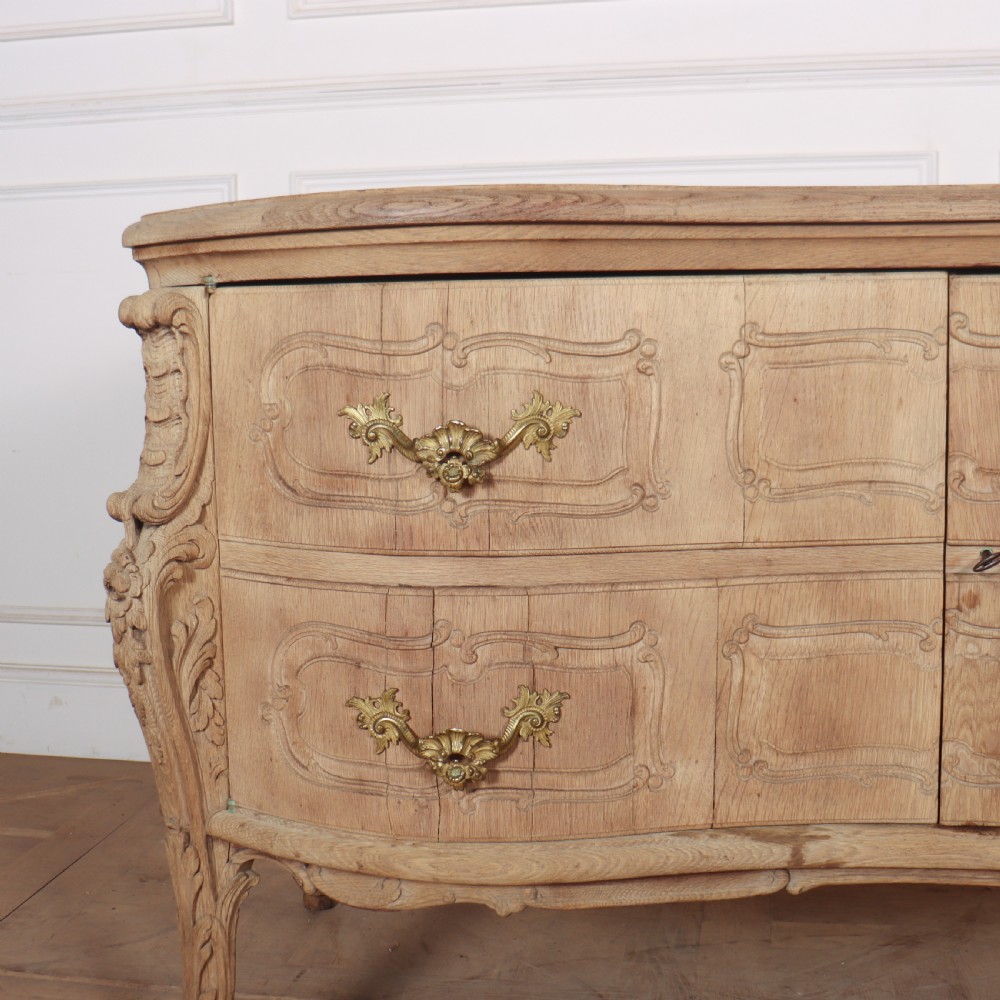 An antique French bleached oak commode featuring a serpentine front, carved rocaille mouldings, drawers with brass pulls, and cabriole feet. View III