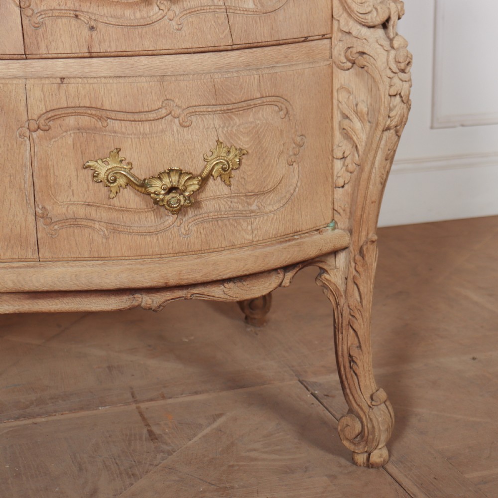 An antique French bleached oak commode featuring a serpentine front, carved rocaille mouldings, drawers with brass pulls, and cabriole feet. View IV