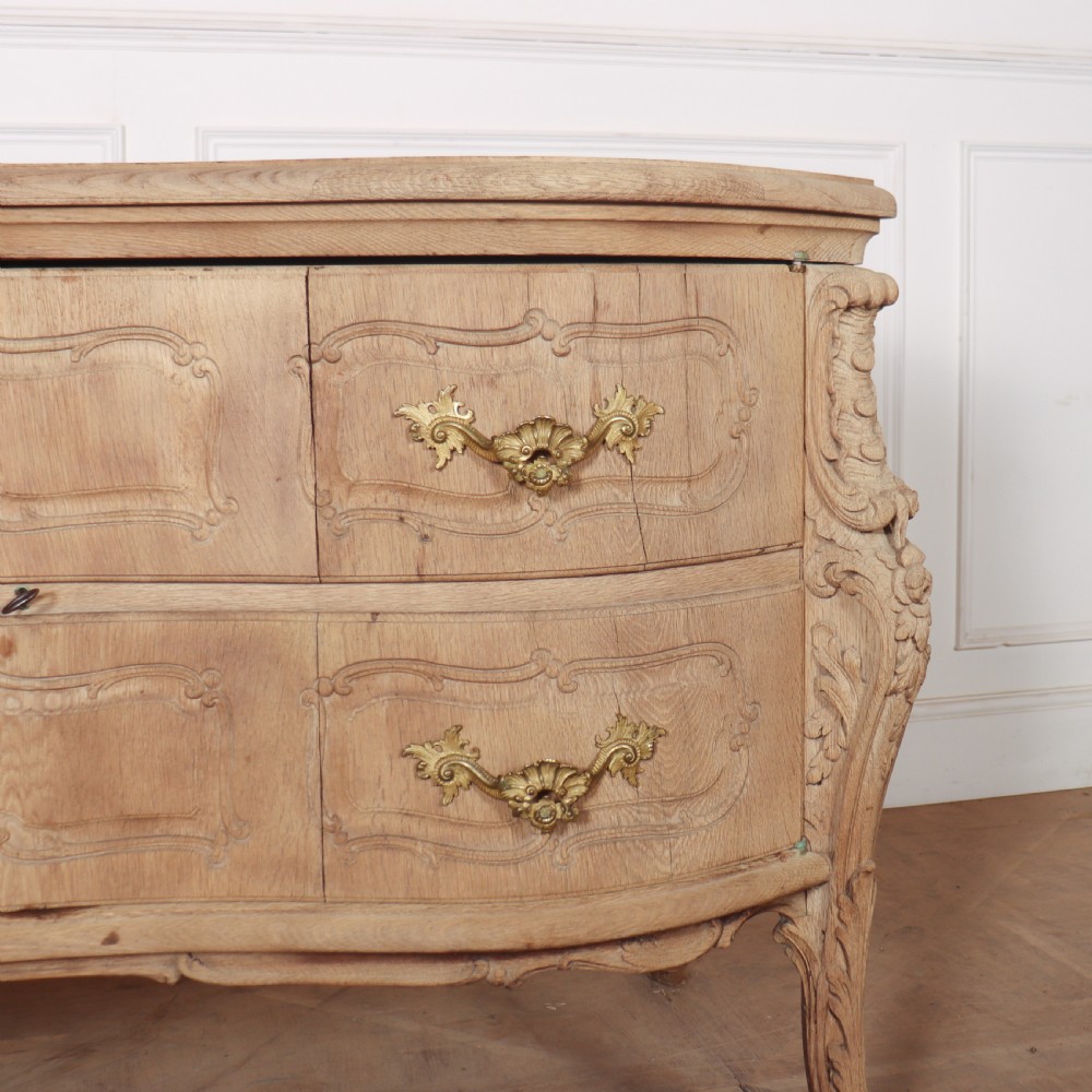 An antique French bleached oak commode featuring a serpentine front, carved rocaille mouldings, drawers with brass pulls, and cabriole feet. View V