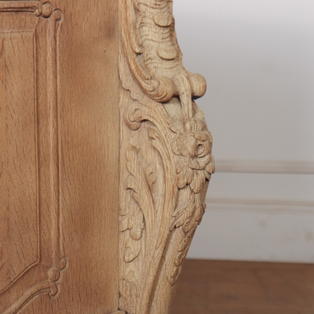 An antique French bleached oak commode featuring a serpentine front, carved rocaille mouldings, drawers with brass pulls, and cabriole feet. View IX