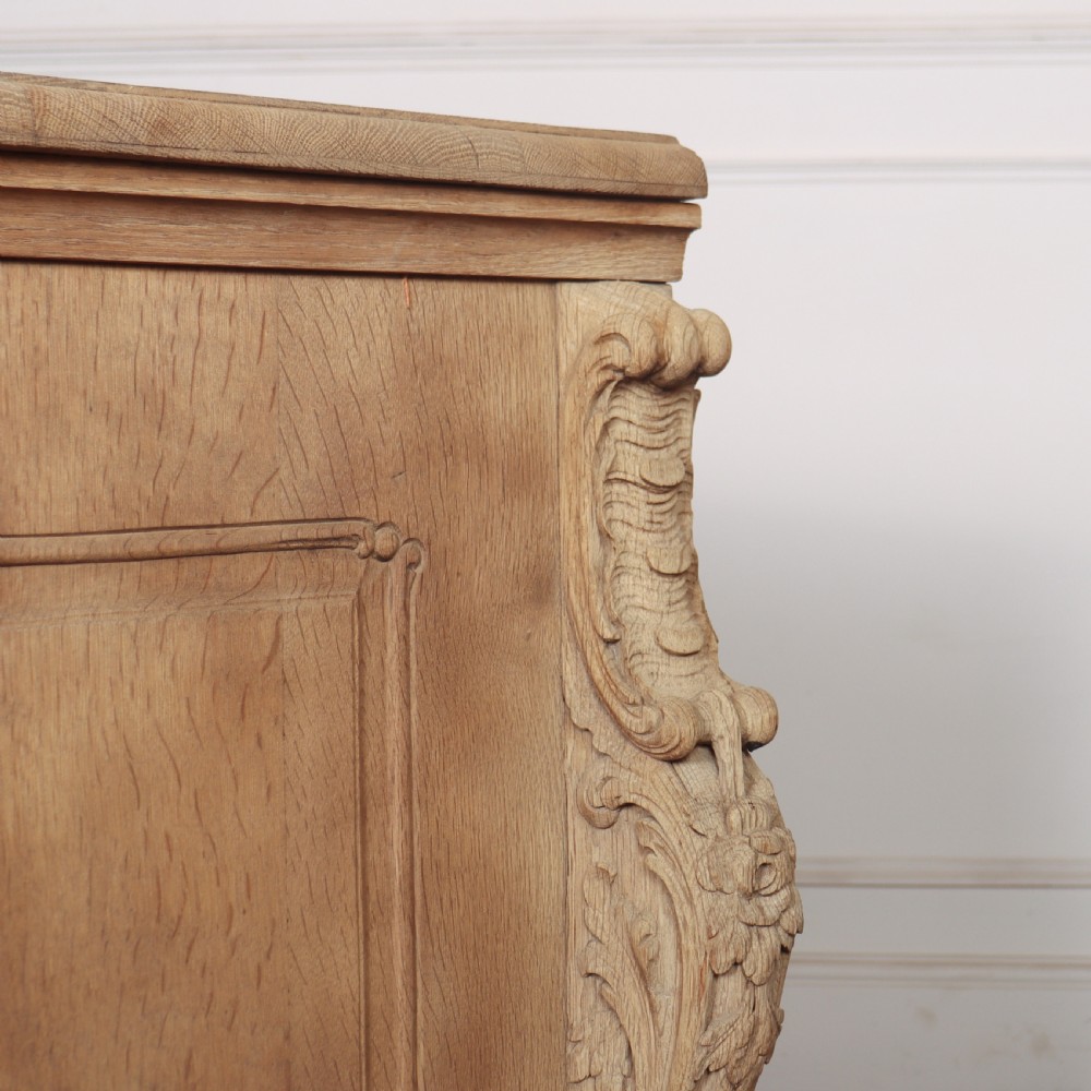 An antique French bleached oak commode featuring a serpentine front, carved rocaille mouldings, drawers with brass pulls, and cabriole feet. View XI