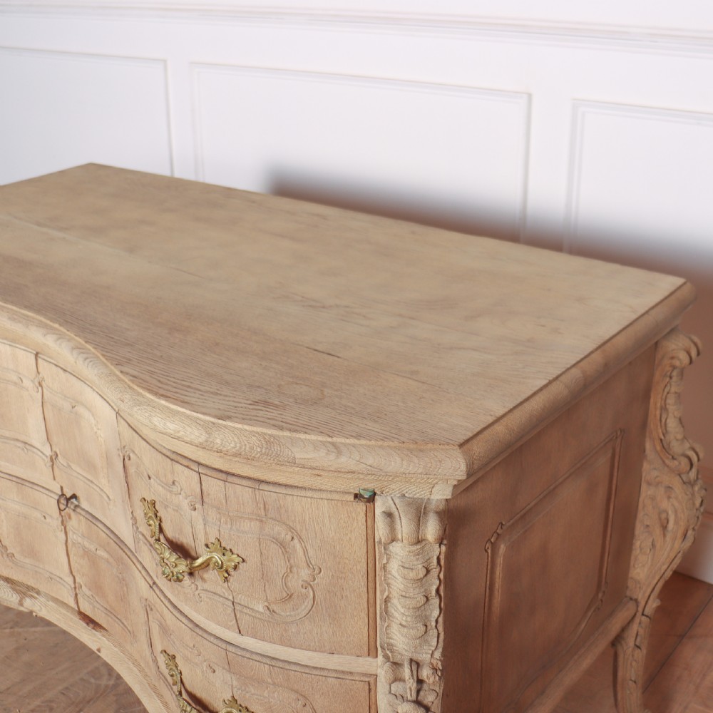 An antique French bleached oak commode featuring a serpentine front, carved rocaille mouldings, drawers with brass pulls, and cabriole feet. View XII