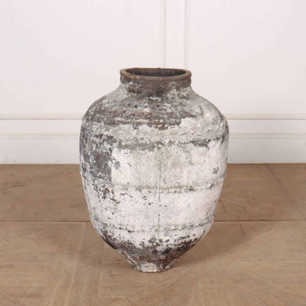 A large, tapered terracotta olive jar featuring a heavily distressed off-white painted surface over dark earthenware clay with a rolled rim.