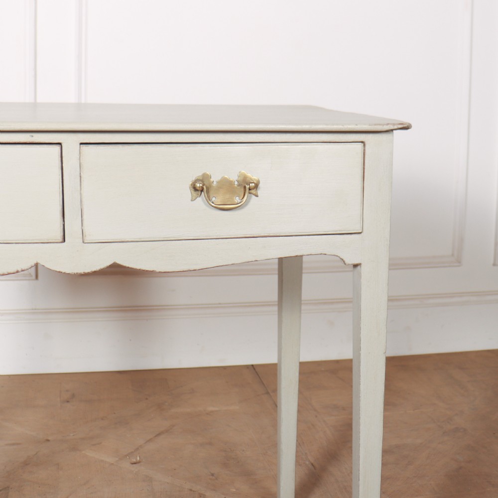 A light grey painted wooden side table featuring two small drawers with brass handles and straight tapered legs against a neutral background. View II