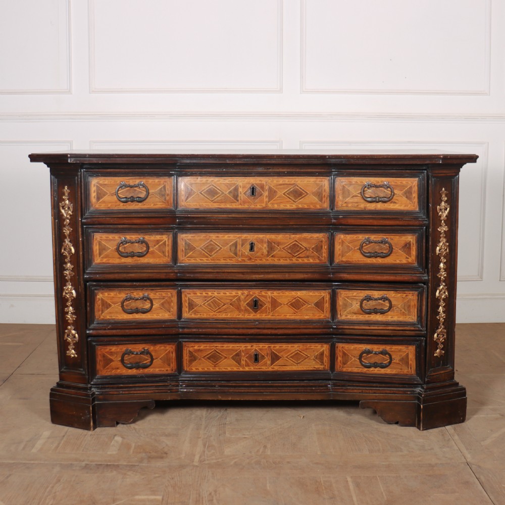 An 18th-century Italian walnut commode featuring four drawers with geometric parquetry inlay and gilt brass pilaster mounts.