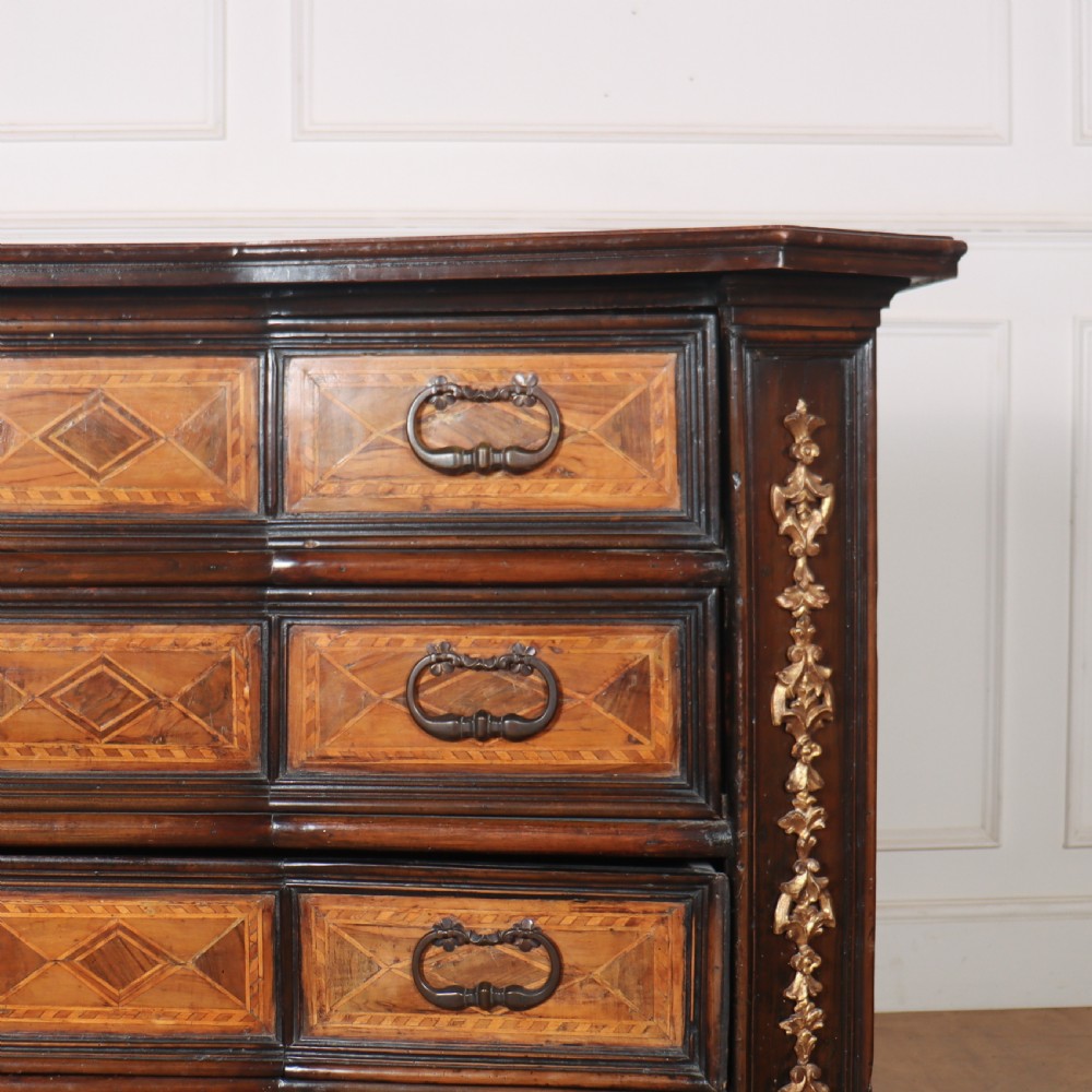 An 18th-century Italian walnut commode featuring four drawers with geometric parquetry inlay and gilt brass pilaster mounts. View V