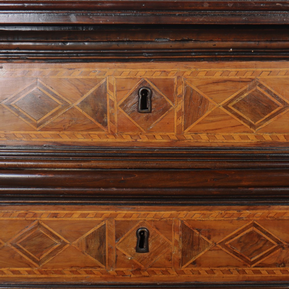 An 18th-century Italian walnut commode featuring four drawers with geometric parquetry inlay and gilt brass pilaster mounts. View VII