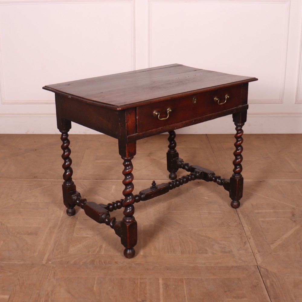 An antique dark oak side table with spiralled barley twist legs, an H-stretcher base, and a single frieze drawer with brass handles.