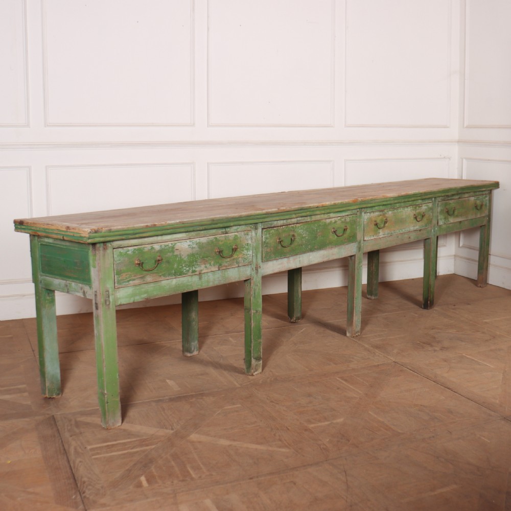 An exceptionally long antique English pine dresser base featuring a distressed green painted finish, four drawers with drop handles, and an unpainted timber top surface.