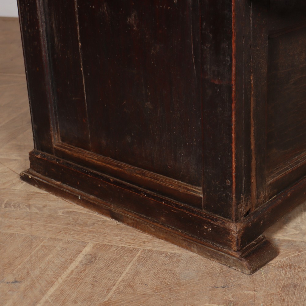 A dark stained oak corner bacon settle featuring high panelled cupboard doors, upper drawers with brass handles, and an integrated bench seat. View IV