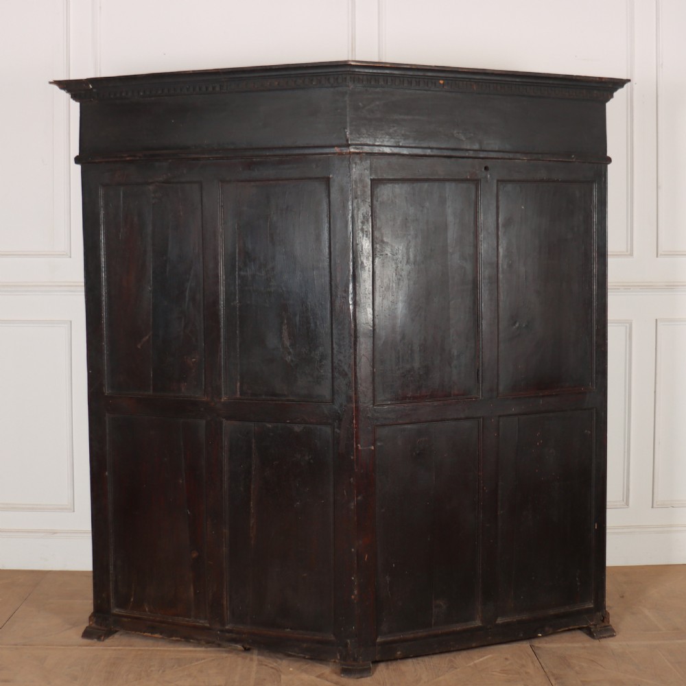 A dark stained oak corner bacon settle featuring high panelled cupboard doors, upper drawers with brass handles, and an integrated bench seat. View VII