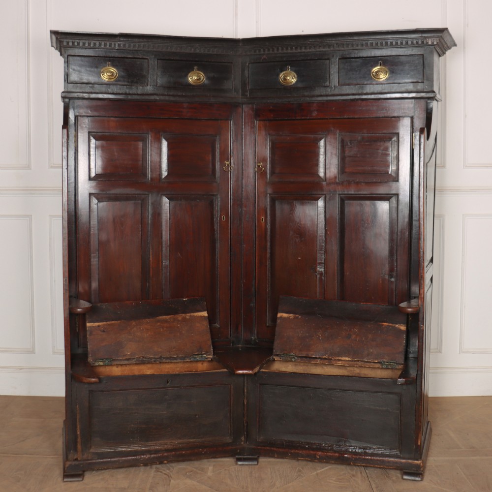 A dark stained oak corner bacon settle featuring high panelled cupboard doors, upper drawers with brass handles, and an integrated bench seat. View VIII