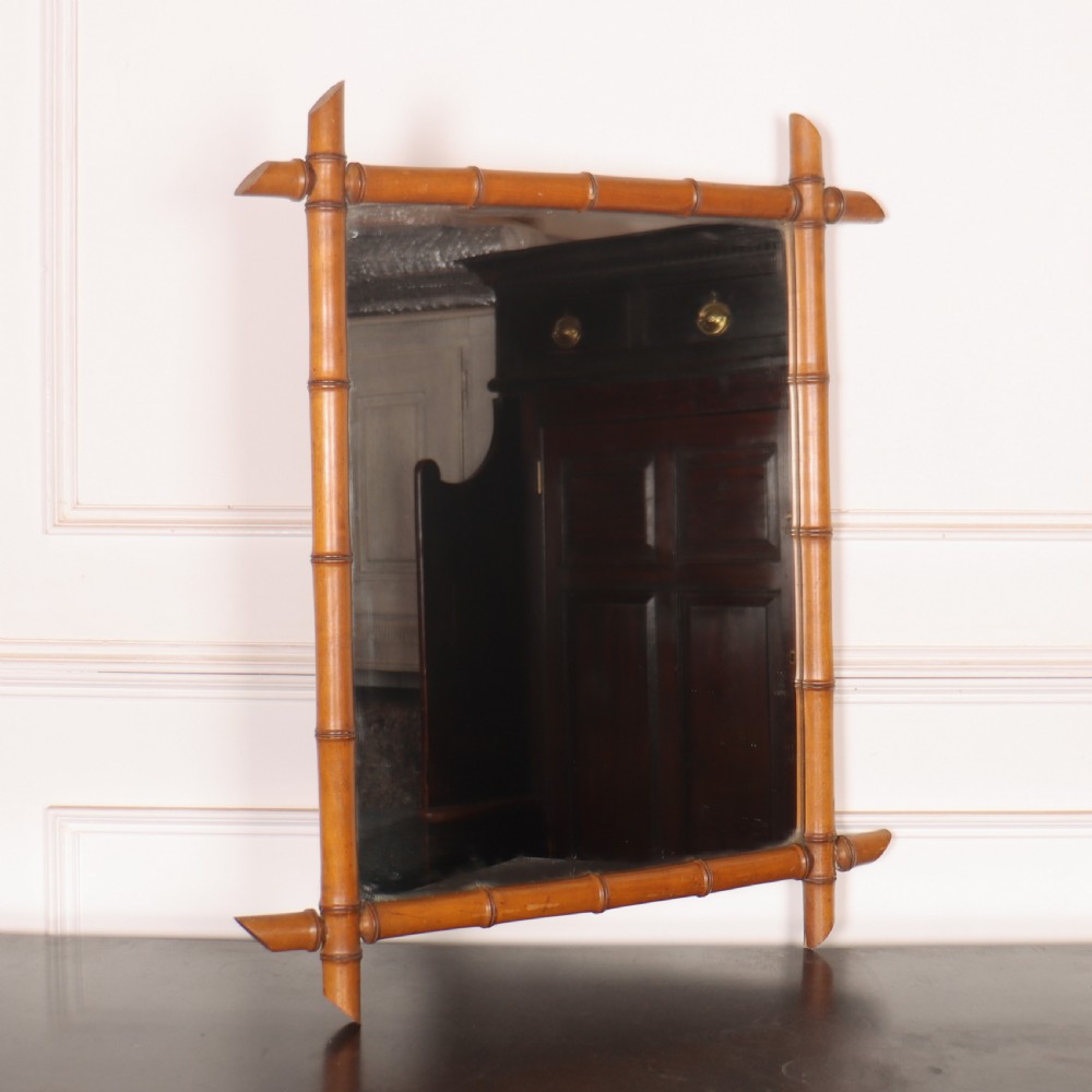 A rectangular wall mirror with a carved wooden frame styled to imitate bamboo, featuring crossed corner joints and a polished honey brown finish.
