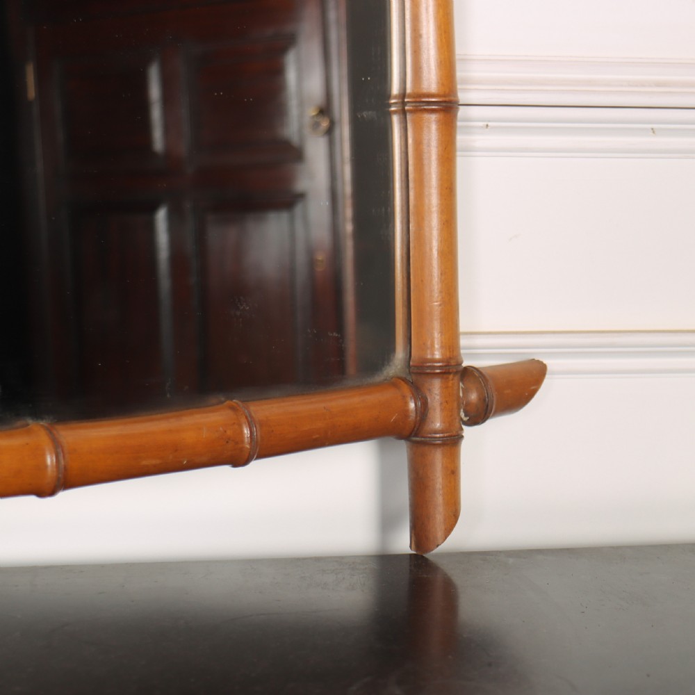 A rectangular wall mirror with a carved wooden frame styled to imitate bamboo, featuring crossed corner joints and a polished honey brown finish. View III