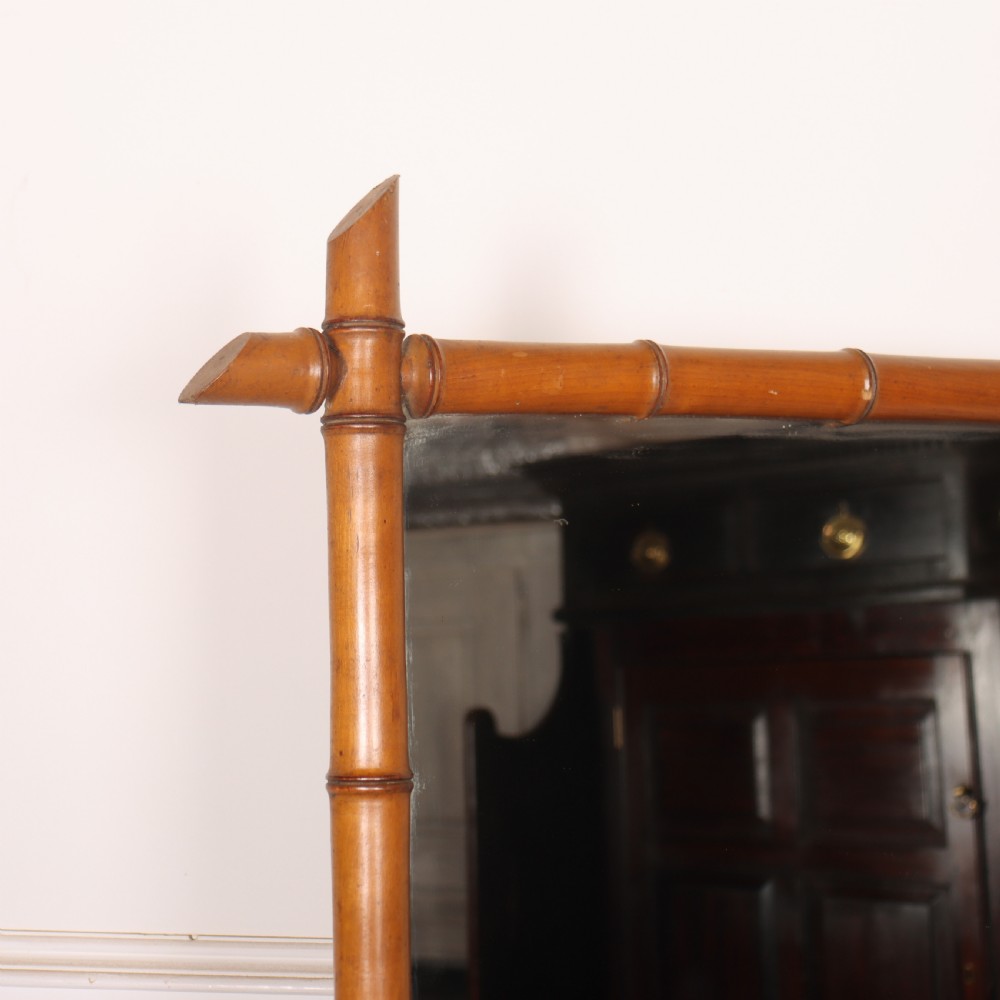 A rectangular wall mirror with a carved wooden frame styled to imitate bamboo, featuring crossed corner joints and a polished honey brown finish. View V