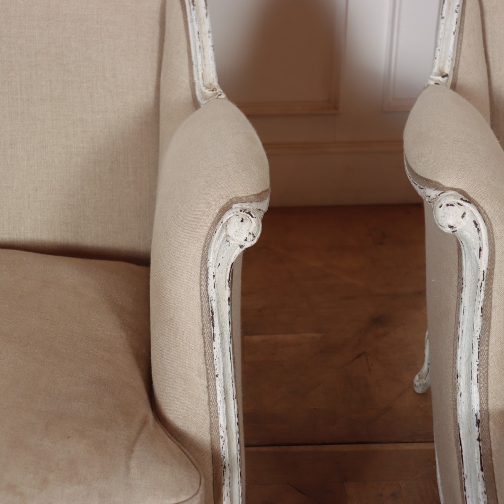 A pair of Swedish Gustavian style armchairs featuring distressed white painted carved wooden frames and beige linen upholstery. View II