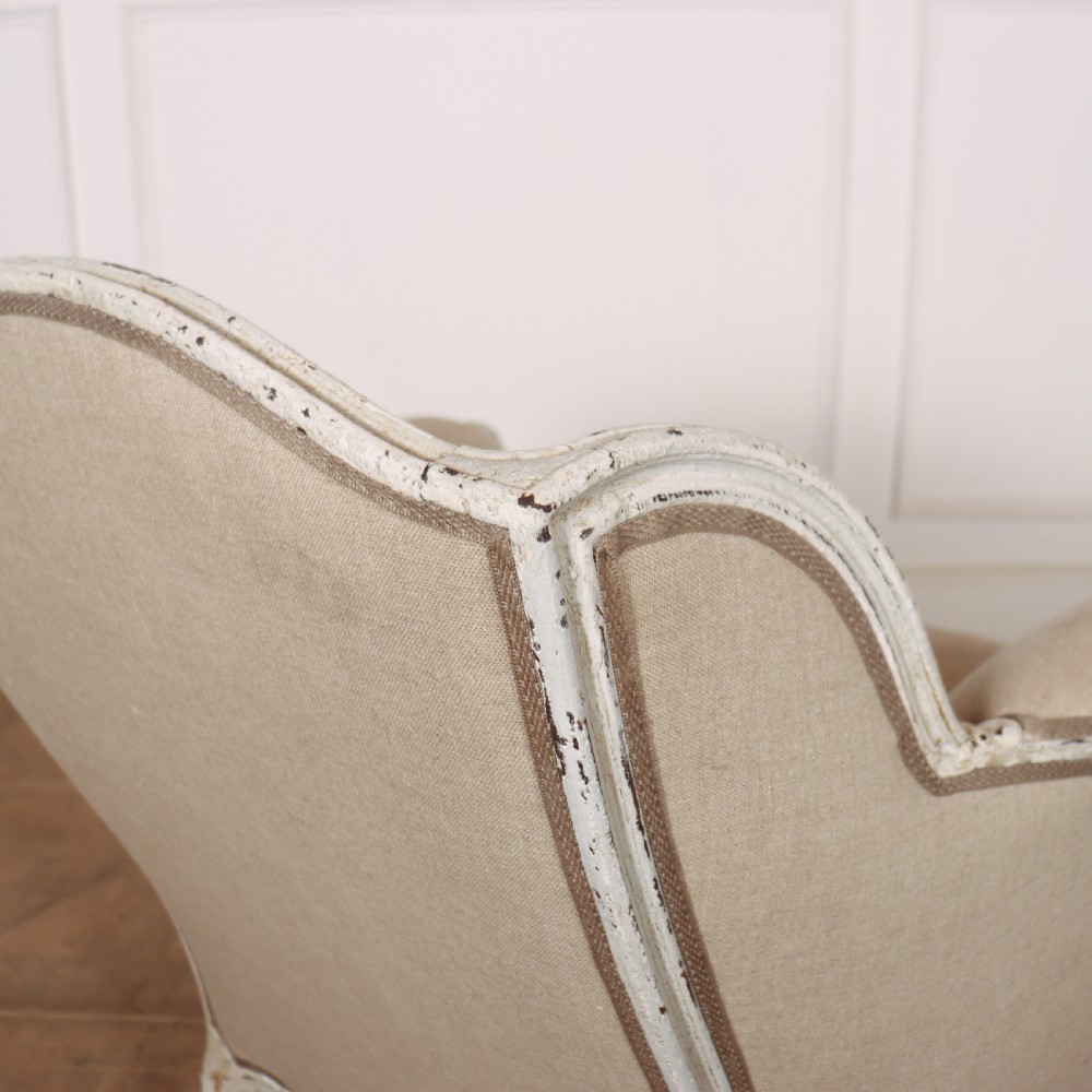 A pair of Swedish Gustavian style armchairs featuring distressed white painted carved wooden frames and beige linen upholstery. View VI