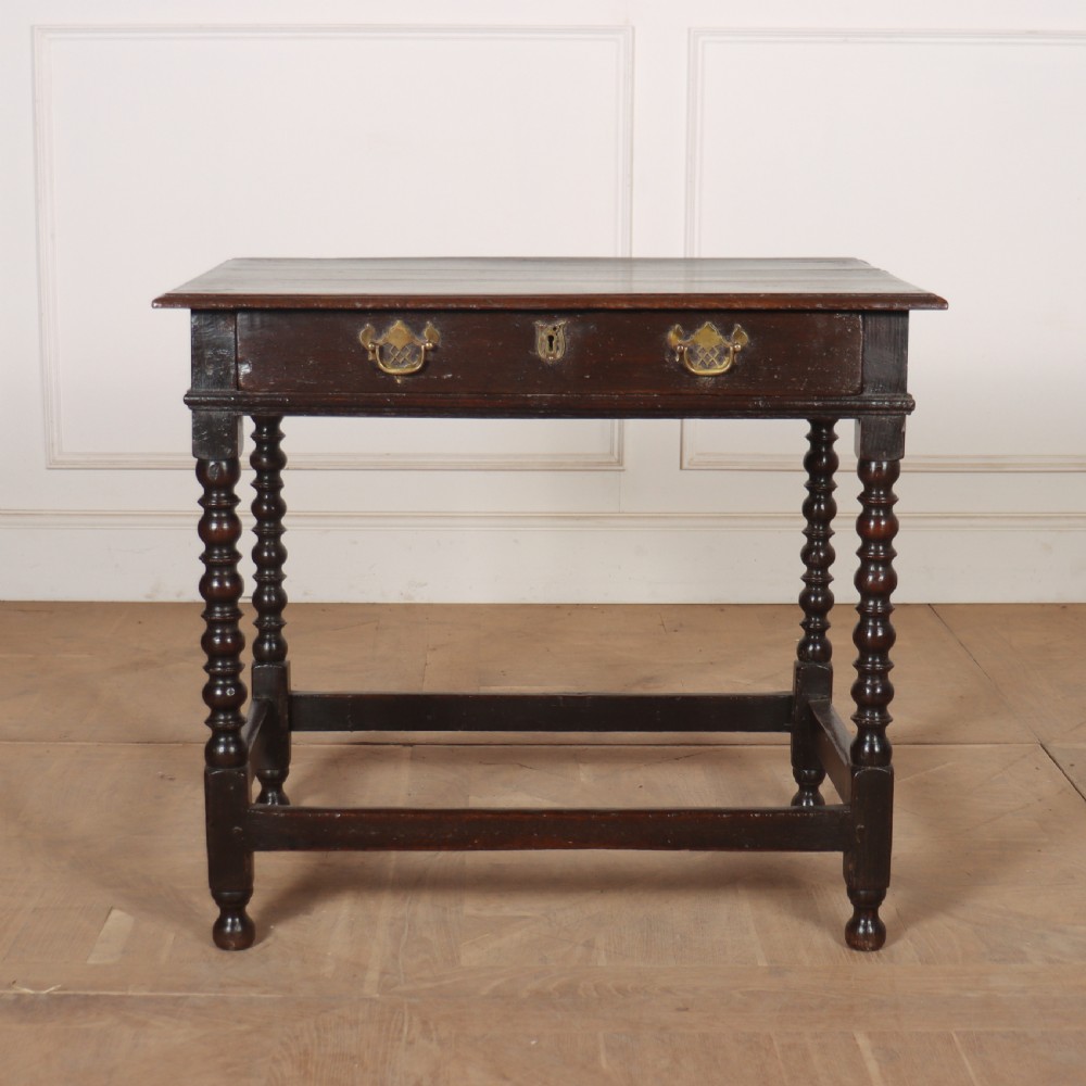 An 18th-century dark oak side table featuring a rectangular top, single drawer with brass handles, bobbin turned legs, and a box stretcher base.