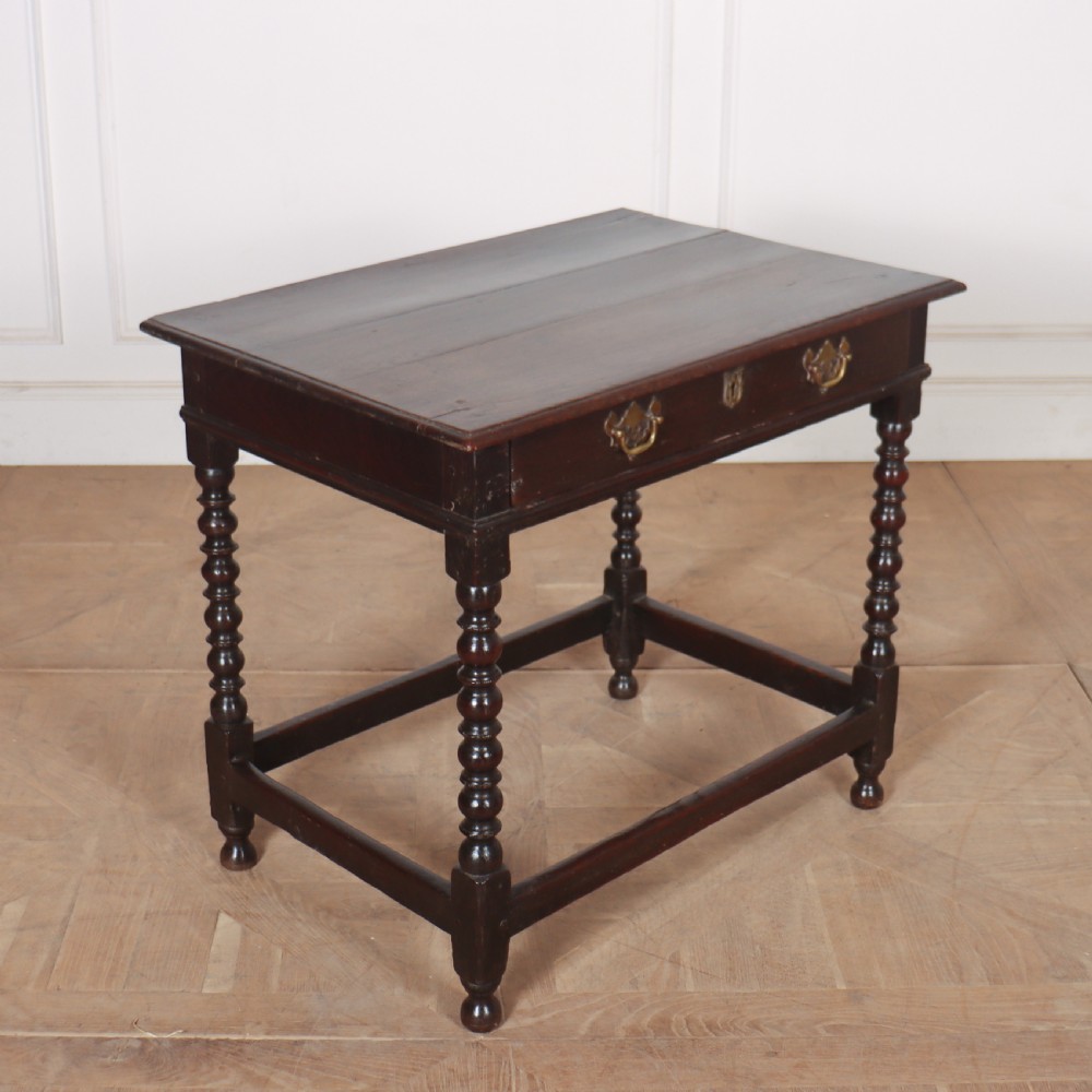 An 18th-century dark oak side table featuring a rectangular top, single drawer with brass handles, bobbin turned legs, and a box stretcher base. View V