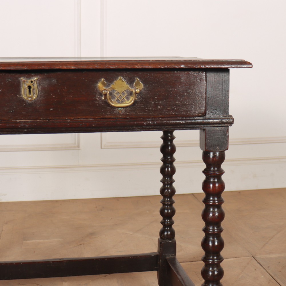 An 18th-century dark oak side table featuring a rectangular top, single drawer with brass handles, bobbin turned legs, and a box stretcher base. View VI