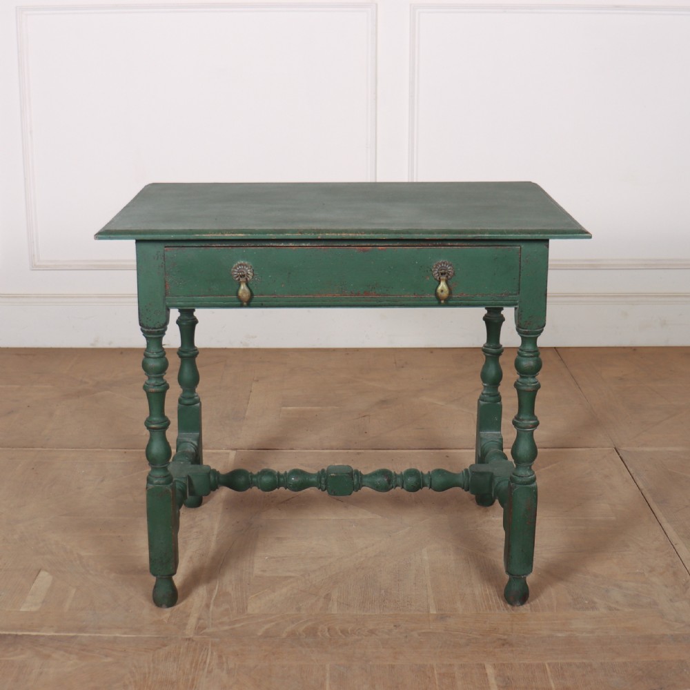 An 18th-century English lamp table featuring a dark green painted surface, single drawer with brass handles, and turned legs with lower stretchers.