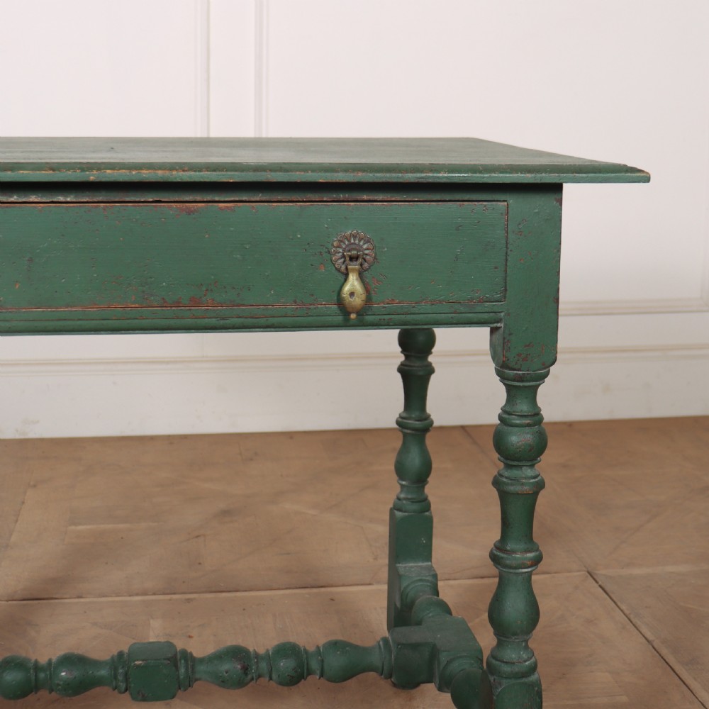 An 18th-century English lamp table featuring a dark green painted surface, single drawer with brass handles, and turned legs with lower stretchers. View V