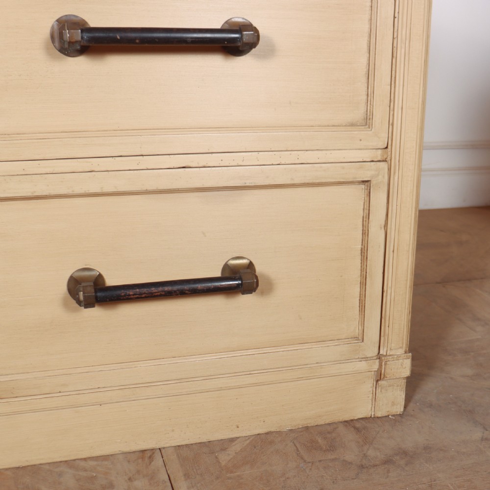 A low, wide wooden drapers chest in a neutral beige painted finish featuring four large paneled drawers with dark metal handles. View V