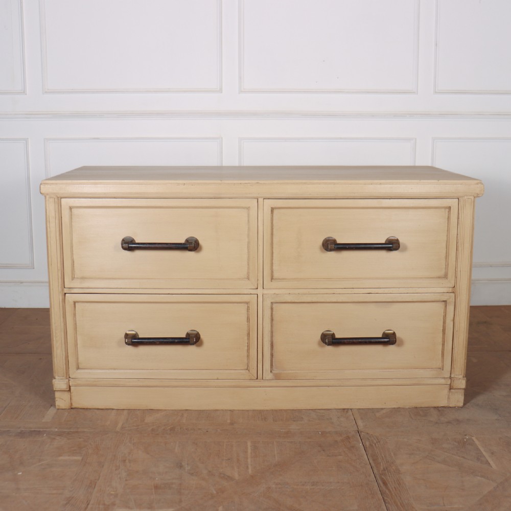 A low, wide wooden drapers chest in a neutral beige painted finish featuring four large paneled drawers with dark metal handles. View VI