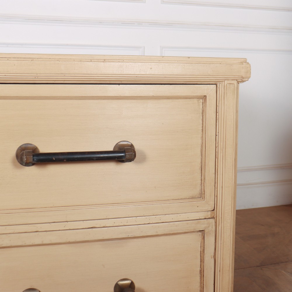 A low, wide wooden drapers chest in a neutral beige painted finish featuring four large paneled drawers with dark metal handles. View VII